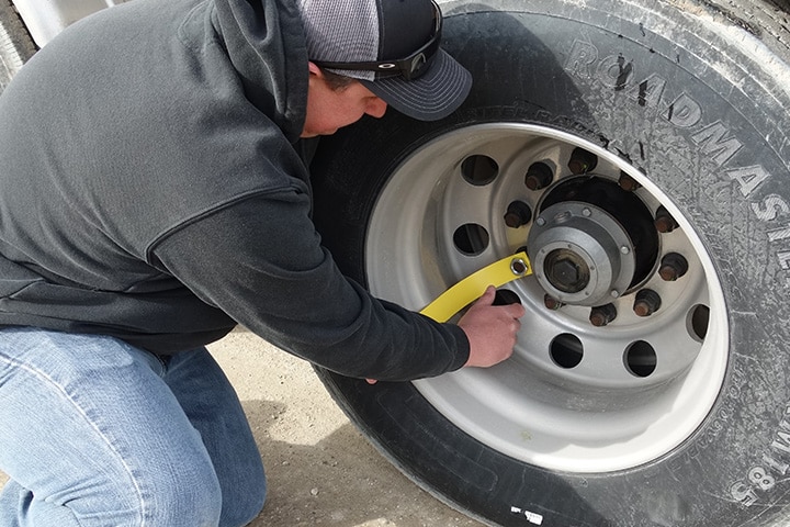 A driver crouches beside a truck, focused on fixing or adjusting a tire along the roadside.